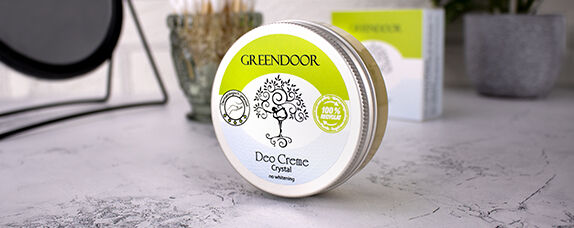 GREENDOOR Deo Creme Crystal auf einem Tisch Eine Dose GREENDOOR Deo Creme Crystal mit 100% natürlichen Inhaltsstoffen auf einem Tisch, umgeben von weiteren Pflegeprodukten.