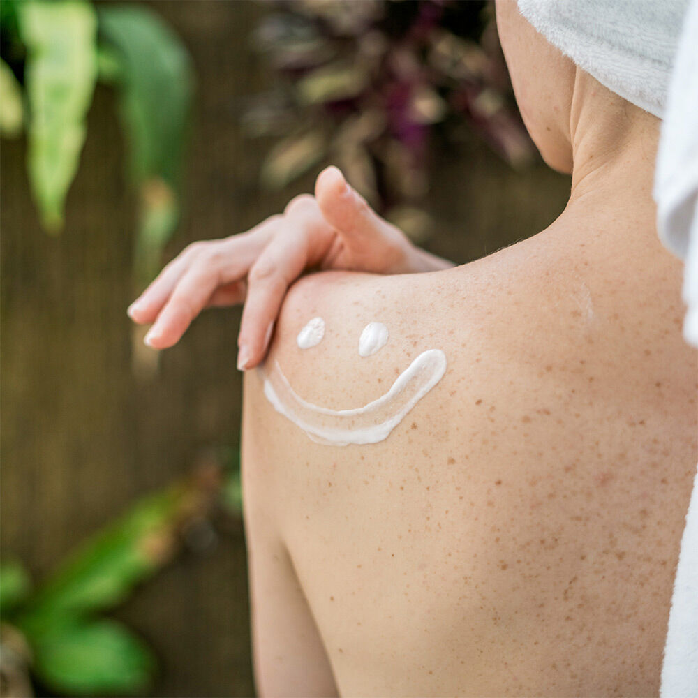 Frauenschulter mit Smiley aus Bodylotion auf der Haut