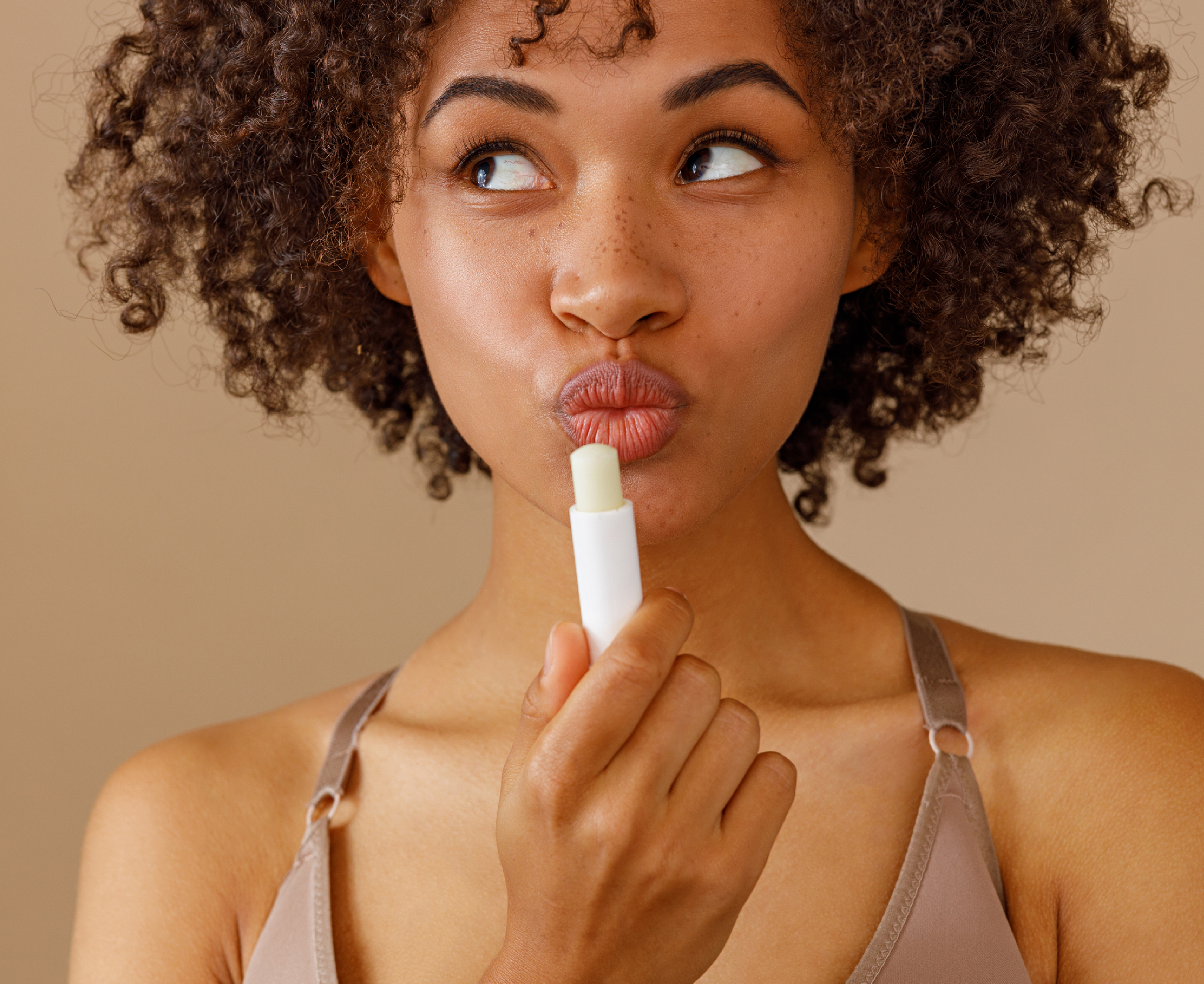 Mythen_der_Lippenpflege Junge Frau mit Locken cremt sich die Lippen mit einem Lippenpflegestift